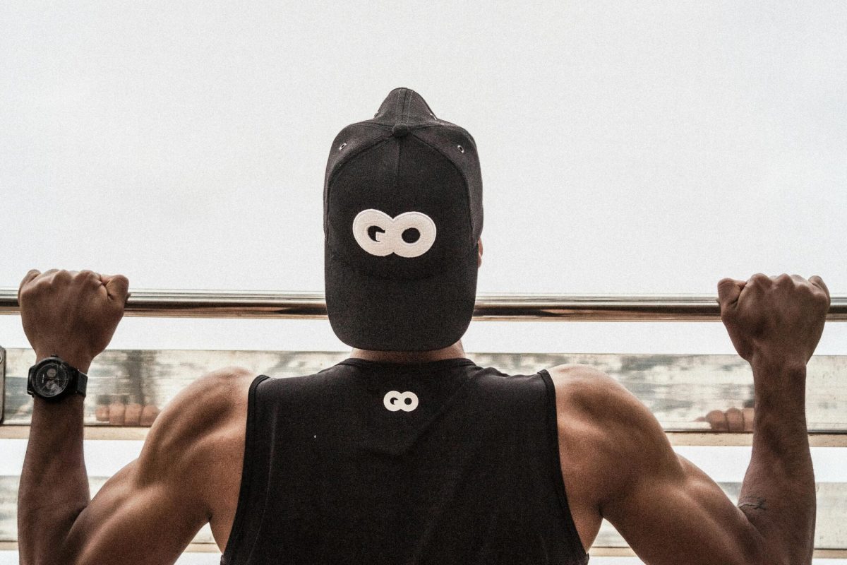 Back view of a man in gym attire doing pull-ups outdoors, demonstrating strength and fitness.